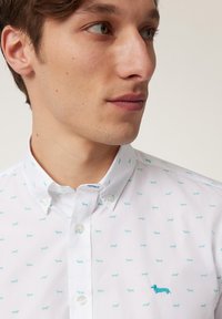 Camisa de algodón blanca con patrones de dachshund en azul claro, cuello abotonado y un dachshund bordado en azul claro en el pecho.