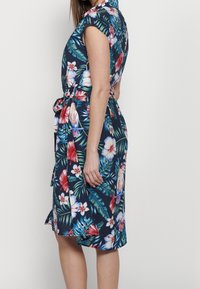 Blumenkleid mit navyblauem Hintergrund, lebhaften roten und weißen Blumen, kurzen Ärmeln und einem gebundenen Bund für eine verstellbare Passform.