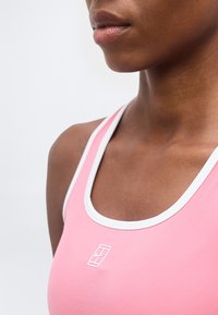 Κοντινό πλάνο ενός ατόμου που φοράει ροζ αθλητικό τοπ με άσπρη επένδυση, δείχνοντας το ντεκολτέ και μερικό πρόσωπο και ώμο.