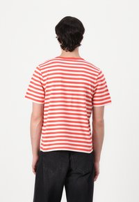 Tricou cu mânecă scurtă în dungi roșii și albe, cu un guler rotund, din material de bumbac, cu o croială lejeră și tiv drept.