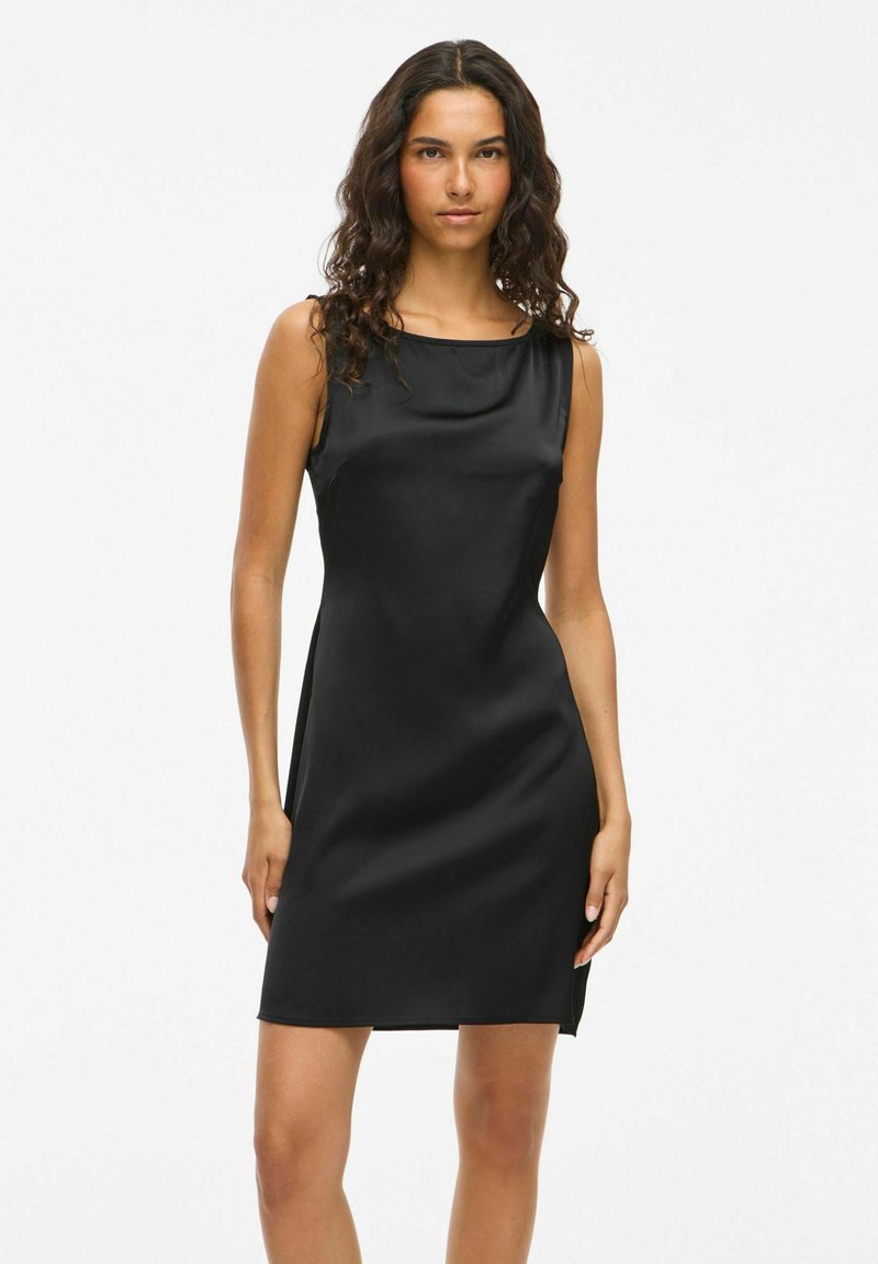 Robe noire sans manches avec une texture satinée lisse, un design ajusté et une coupe longueur genoux, avec une fente latérale subtile pour faciliter les mouvements.