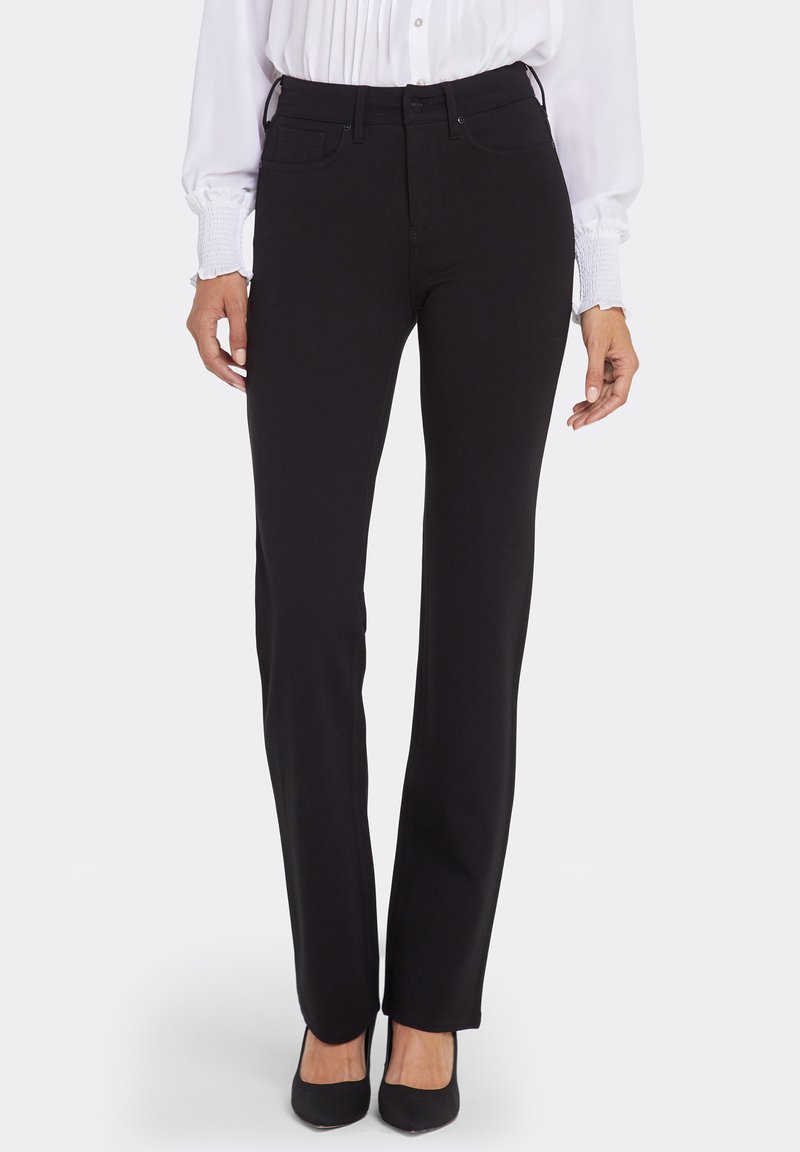 Svarta jeansbyxor i rak modell med framfickor och ett säkerställt midjeband, kombinerade med en vit blus med långa ärmar.