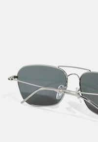 Square-frame sunglasses with grey tinted lenses, a thin silver metal frame, and adjustable nose pads.