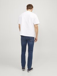 Tricou alb cu mâneci scurte, blugi din denim, pantofi casual. Vedere din spate care arată un design simplu, formă ajustată și culori uni. Fără modele sau accente.