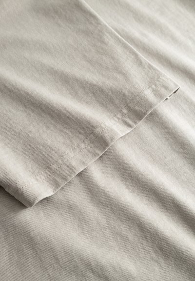 Gros plan sur un tissu en coton beige clair montrant des coutures détaillées sur un bord plié, mettant en valeur la texture et la qualité de la couture.