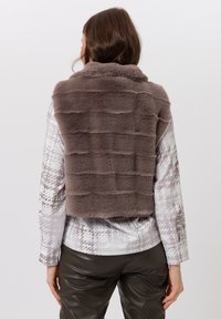 Brown faux fur vest with a textured pattern, featuring horizontal lines; worn over a patterned shirt and dark leather pants.