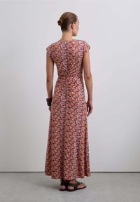 Maxi abito con maniche a cappuccio, realizzato in un tessuto con motivo nei toni del rosa, arancione e marrone, con dettaglio arricciato sul retro, abbinato a sandali marroni.