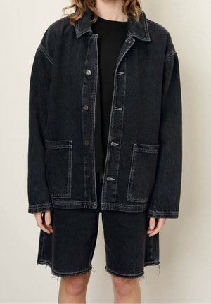 Person iført oversized sort denimjakke med store forlommer og matchende denimshorts med frynset kant.