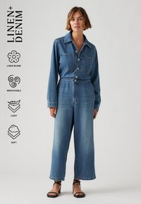 Salopette en denim à manches longues, fermeture à boutons sur le devant, deux poches poitrine, coupe large et délavage bleu clair ; comprend un mélange de lin.