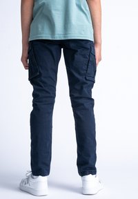 Námořnické cargo kalhoty s několika bočními kapsami, zúženými nohavicemi a lehkým materiálem, spárované s bílými teniskami a světle modrou košilí.