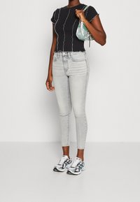Top corto negro de canalé con costuras blancas, jeans skinny de tiro alto en un gris claro, y zapatillas blancas con acentos en gris y teal.