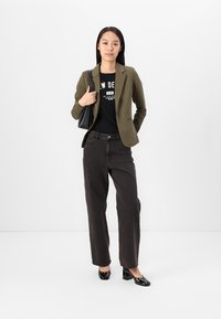 Olivgrön kavaj över en svart grafisk t-shirt, i kombination med svarta vida jeans och svarta lackläderklackar. Enkel handväska.