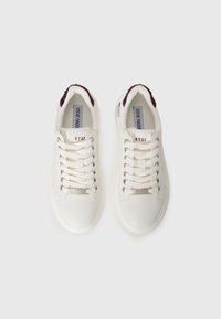 Hvide sneakers med snørredesign, teksturerede maroon accenter ved hælen, sølvhardware og en flad gummisål. Mærkets logo er synligt på tungen.