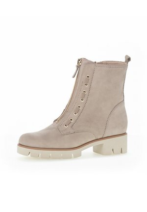 Beige suede ankle boot with gold zipper, lace-up front, textured upper, and chunky white sole. Features pull tab at the heel.