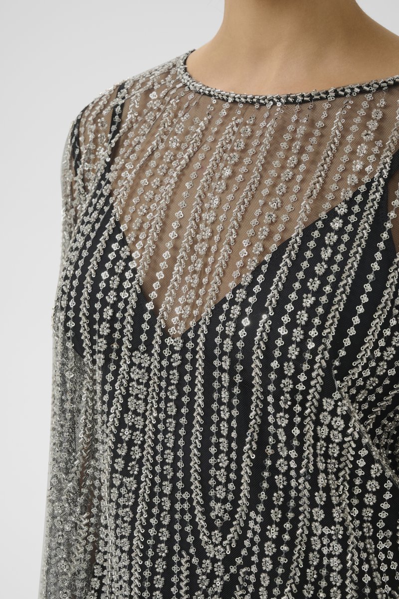 Black dress with sheer beaded overlay featuring silver accents in a vertical pattern. Notable details include a rounded neckline and intricate textures.