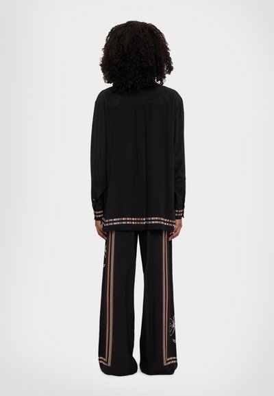 Black long-sleeve shirt with a colorful striped trim and embroidered details, paired with wide-leg black pants featuring similar accents.