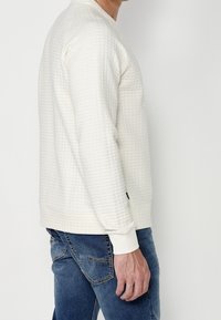 Pullover crema a maglia con superficie texturizzata e trapuntata, maniche e orlo a costine, abbinato a jeans in denim blu.