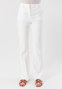 Pantaloni bianchi a vita alta con una vestibilità slim e un leggero svaso, realizzati in un tessuto morbido e con pieghe frontali pulite; abbinati a sandali marroni.
