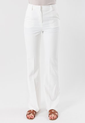 Pantaloni bianchi a vita alta con una vestibilità slim e un leggero svaso, realizzati in un tessuto morbido e con pieghe frontali pulite; abbinati a sandali marroni.