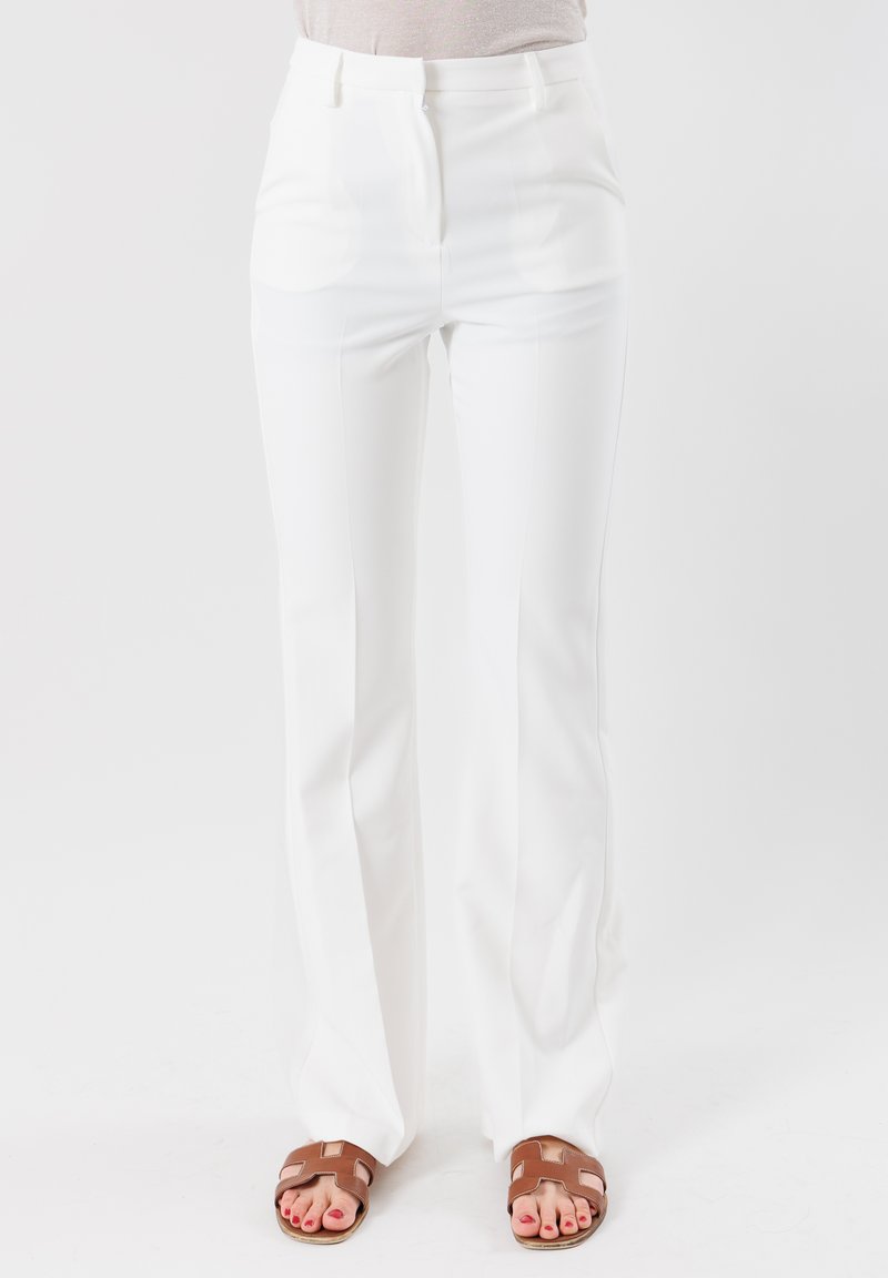 Pantaloni bianchi a vita alta con una vestibilità slim e un leggero svaso, realizzati in un tessuto morbido e con pieghe frontali pulite; abbinati a sandali marroni.