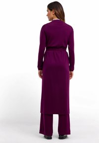 Robe en maille longue, violette, avec des manches longues, une taille ceinturée et un design superposé allant jusqu'aux chevilles, dotée d'une texture lisse.