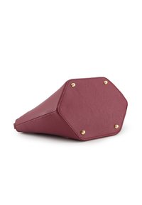 Sac en cuir bordeaux hexagonal avec une surface texturée, pieds en métal doré à la base et un design épuré et minimaliste.