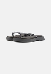 Mustad mustikudega mustad kummist plätud, millel on tekstureeritud rihm ja lame tald. Kujundus on minimalistlik ja siledapinnaline.
