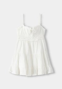 Vit ärmlös sommarklänning med tunna band, åtsittande rynkad livstycke, knytning i mitten och flera lager volanger i nederkanten.