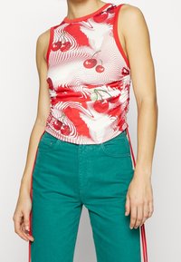 Rood tanktop met kerspatroon, ronde halslijn, mouwloos ontwerp, geplooide zijkanten en een gestructureerde grafische print, gecombineerd met groene broek.