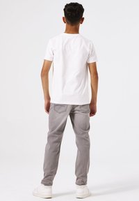 Camiseta blanca de manga corta combinada con jeans de color gris claro. Los jeans tienen dos bolsillos traseros con un diseño de costura sutil. Zapatillas blancas completan el atuendo.