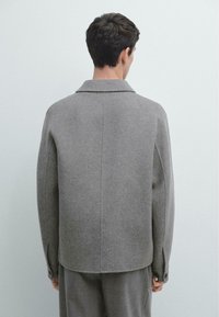 Grå jakke i uldblanding med en afslappet pasform, hakket krave og manchetter med knapper. Glat tekstur, minimalistisk design og rene linjer.