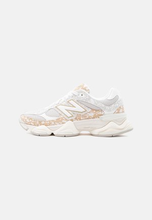 Weißer und beiger New Balance Sneaker mit Mesh-Einsätzen, Sprenkelmuster-Akzenten und gepolsterter Sohle, seitlich auf einem schlichten Hintergrund gesehen.