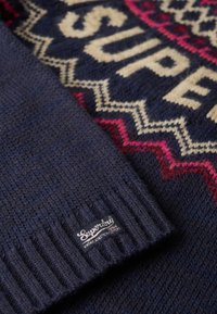 Maglione navy a maglia con motivo geometrico in crema e rosa. Presenta polsini a coste e un'etichetta con il brand sull'orlo.