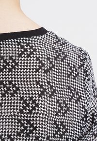 Un tissu noir et blanc à motifs présente un design pied-de-poule, avec un col noir côtelé. La texture semble douce et lisse.