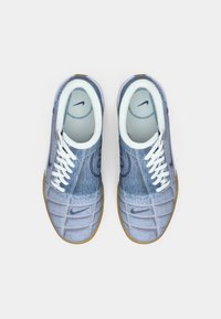 Pár modrých tenisek s deninovým texturou značky Nike, s bílými tkaničkami a světle hnědými podrážkami, pohled shora na bílém pozadí.