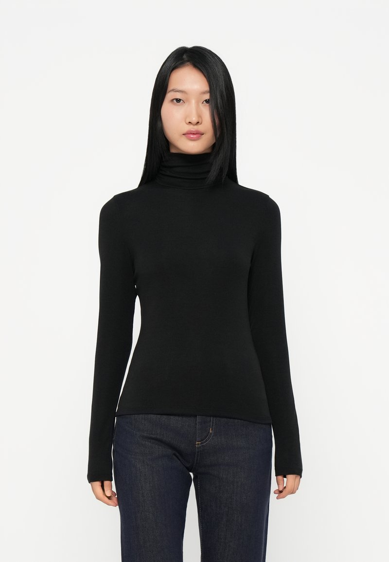 Schwarzer Rollkragenpullover mit langen Ärmeln, aus glattem Stoff gefertigt. Figurbetonte Silhouette, minimalistisches Design, kombiniert mit dunkelblauen Jeans.