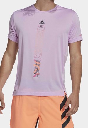 Homme portant un t-shirt de trail Adidas Terrex violet clair et un short orange vif avec des rayures noires sur la jambe droite.
