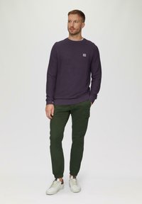 Paarse textured trui met ronde hals, gecombineerd met groene cargo broek en witte sneakers. Opvallend klein logo op de trui.