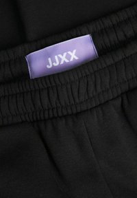 Black sweatpants with a ribbed waistband, featuring a light purple label that reads "JJXX," highlighting soft cotton fabric.