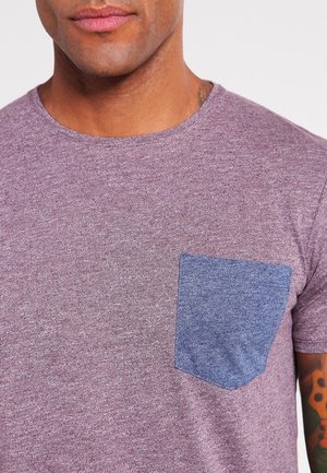 Lilla kortærmet t-shirt lavet af tekstureret stof, med en ensfarvet blå lomme på venstre side.