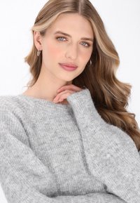 Pulover tricotat de culoare gri deschis, cu decolteu larg și mâneci lungi, realizat dintr-un material moale și texturat. Modelul se atinge ușor de gât.