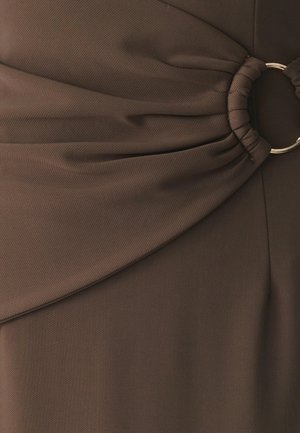 Smeđi materijal s teksturiranom površinom, s nabranim dizajnom i zlatnim prstenom kao naglaskom u struku, što odjeći dodaje dimenziju.