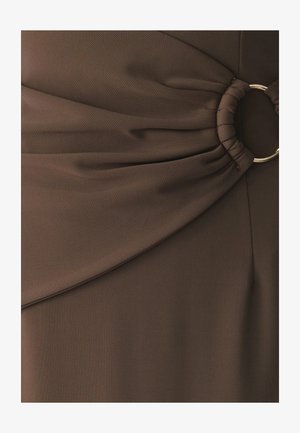 Smeđi materijal s teksturiranom površinom, s nabranim dizajnom i zlatnim prstenom kao naglaskom u struku, što odjeći dodaje dimenziju.