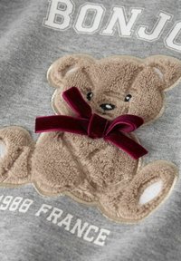 Šedá mikina s hnědým plyšovým medvídkem s burgundskou sametovou mašlí, vyšitým textem "BONJOUR" a měkkou texturou.