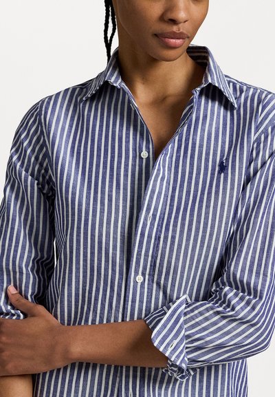 Chemise boutonnée rayée bleue et blanche en lin, avec un col, des manches longues et un petit logo brodé sur la poitrine.