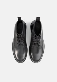 Zapatos de cuero negros con un acabado suave, punteras redondeadas y diseño de cordones. Presenta dos lengüetas en el talón para facilitar su uso.