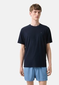 Marineblå kortærmet t-shirt lavet af blødt stof, med rund halsudskæring og et diskret logo på brystet. Sammen med lyseblå shorts.