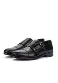 Un par de zapatos de vestir de piel negra con doble hebilla, puntera afilada y hebillas plateadas, mostrados sobre un fondo blanco.