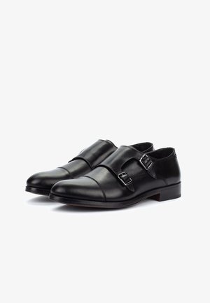 Ein Paar schwarze Leder-Doppel-Monk-Schuhe mit spitzen Zehen und silbernen Schnallen, auf weißem Hintergrund dargestellt.