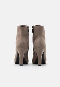 Botas de tobillo de ante marrón con una textura suave, tacones altos de aguja y cremalleras en los laterales. Diseño de punta ligeramente afilada.